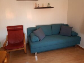 Een kamer met een rode stoel, een blauwe bank met kussens en een houten vloer.