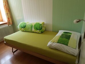 Een eenpersoonsbed met een groene matras en twee kussens, waarvan één met een bladmotief en de ander effen wit.