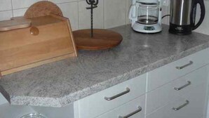 Uma cozinha com cafeteira, chaleira e tábua de corte de madeira no balcão.
