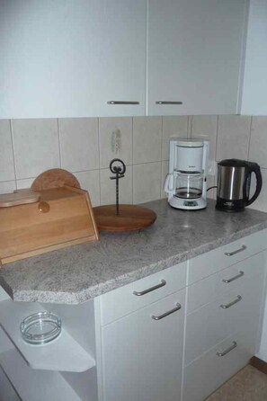 Een keuken met een koffiezetapparaat, een waterkoker en een houten snijplank op het aanrecht.