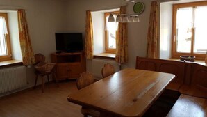 Quarto com uma mesa de jantar de madeira, cadeiras, televisão e uma janela com cortinas.