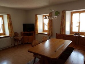 Een kamer met een houten eettafel, stoelen, een televisie en een raam met gordijnen.