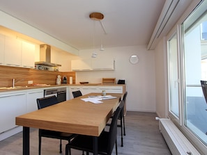 A modern kitchen with a wooden dining table, black chairs, and a large window.