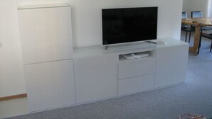 A white entertainment unit with a flat-screen TV, a small shelf, and a drawer. - Tgesa La Niva 1 Appartement/Fewo, Dusche oder Bad, WC, 2 Schlafräume by Interhome (Savognin)