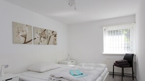 A minimalist bedroom with a bed, bedside tables, a chair, and a window. - Tgesa La Niva 1 Appartement/Fewo, Dusche oder Bad, WC, 2 Schlafräume by Interhome (Savognin)