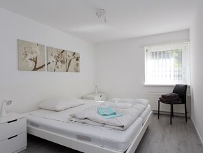 Ein schlicht eingerichtetes Schlafzimmer mit Bett, Nachttischen, einem Sessel und einem Fenster.