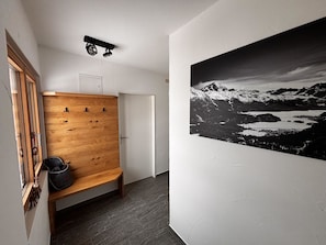 A hallway with a wooden bench, a coat rack, a door, and a large black and white mountain landscape painting on the wall. - Bergnest 4 Appartement/Fewo, Bad, WC, 2 Schlafräume by Interhome (Bivio)
