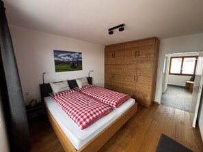 Een slaapkamer met een houten bed, een grote kledingkast, een schilderij aan de muur en uitzicht op buiten.