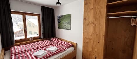 A bedroom with a single bed, a wooden wardrobe, a window with curtains, and a wall-mounted picture.