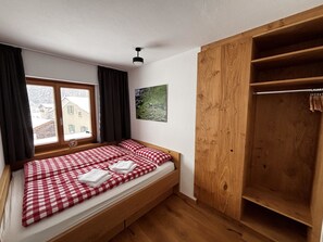 Ein Schlafzimmer mit einem Einzelbett, einem Holzschrank, einem Fenster mit Vorhängen und einem an der Wand hängenden Bild.
