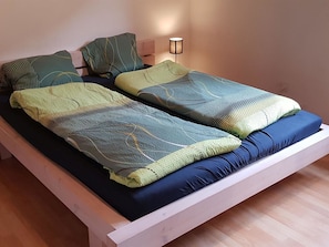 Un lit avec un matelas bleu, deux couvertures vertes et un seul oreiller.
