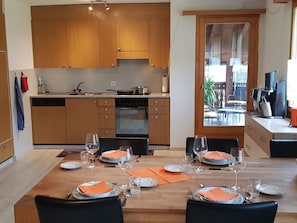 Une cuisine moderne avec des meubles en bois, une table à manger dressée pour quatre personnes, avec des verres à vin et des assiettes, et une machine à café en arrière-plan.
