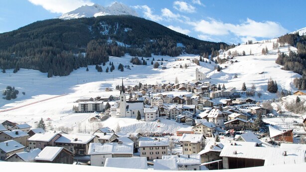 A snow-covered village with traditional buildings, a church, and a mountain in the background.