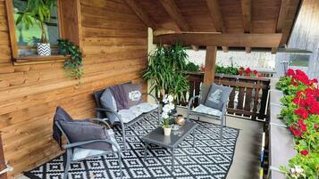 Eine überdachte Terrasse mit zwei Metallstühlen, einem Tisch und einem gemusterten Teppich.