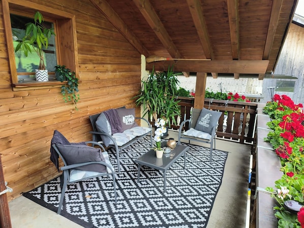 A covered patio with two metal chairs, a table, and a patterned rug.