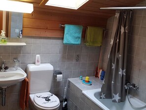 Une salle de bain avec des toilettes, un lavabo et une baignoire. Des serviettes sont accrochées au mur et il y a un rideau de douche.