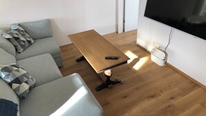Uma sala de estar moderna com um sofá, uma mesa de centro de madeira e uma TV de tela plana fixada na parede.