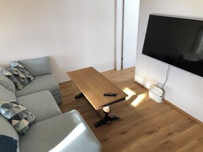 Ein modernes Wohnzimmer mit einer Couch, einem Holztisch und einem flachbildfernseher an der Wand.