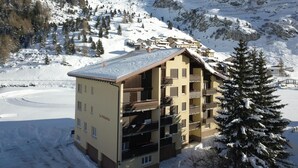 Um hotel com várias andares e varandas, rodeado por montanhas e árvores cobertas de neve.