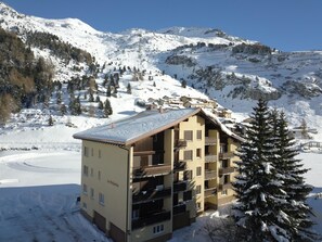 Ein mehrstöckiges Hotel mit Balkonen, umgeben von schneebedeckten Bergen und Bäumen.