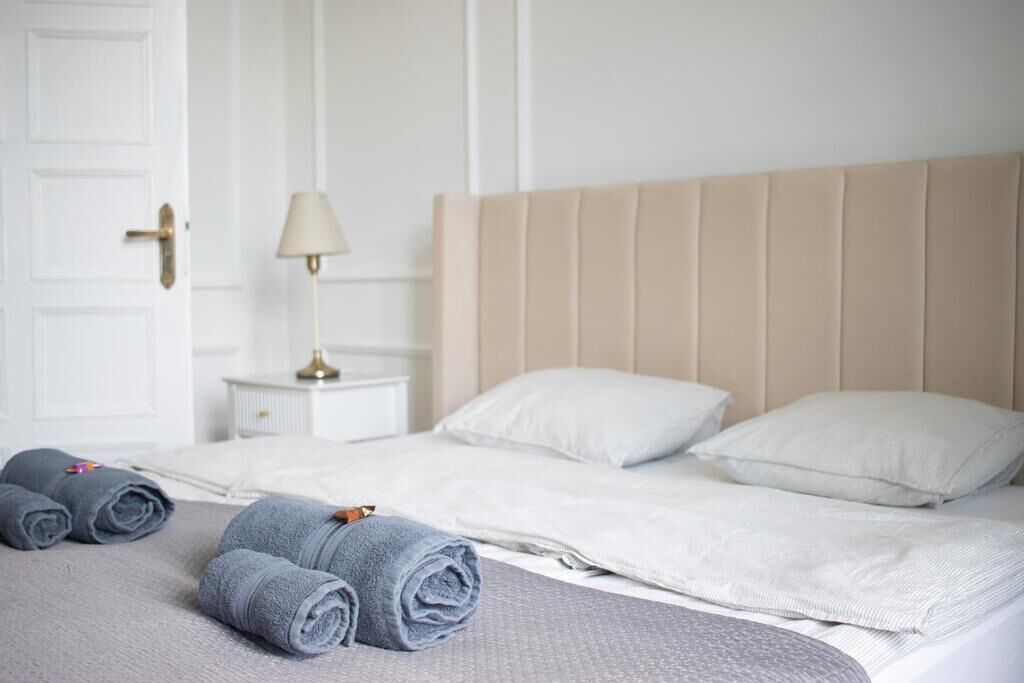 Habitación de hotel con cama, dos almohadas, mesita de noche con lámpara y dos toallas enrolladas.