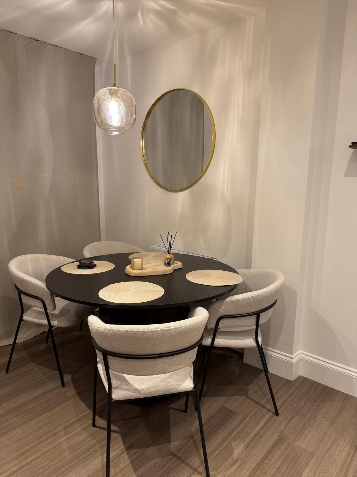 A round dining table with four chairs, a hanging light fixture, and a round mirror on the wall.