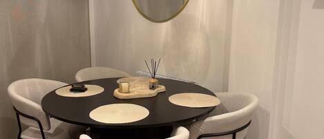 A round dining table with four chairs, a hanging light fixture, and a round mirror on the wall.