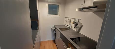 A compact kitchen with a built-in oven, a sink, and a window above the countertop.