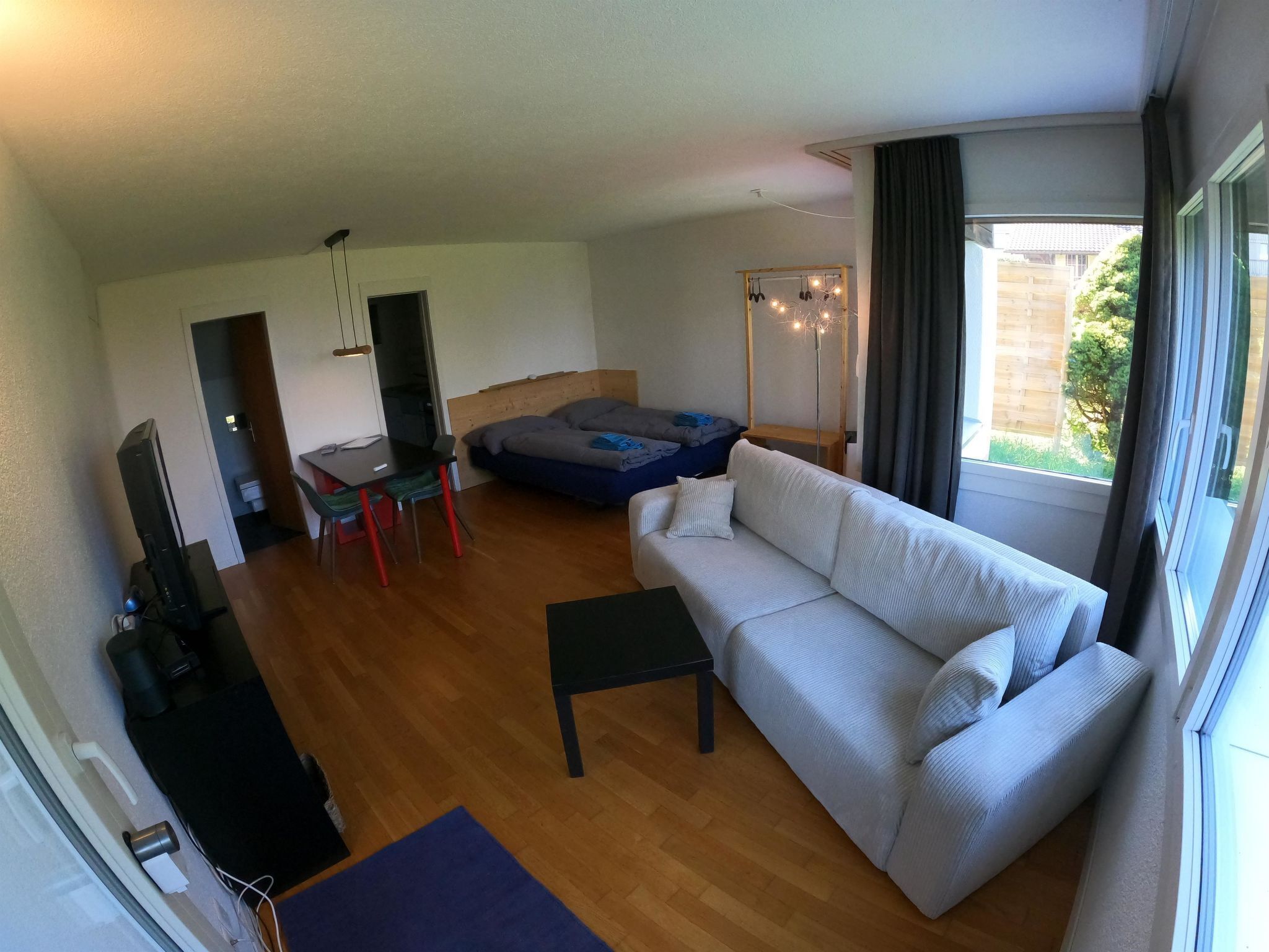 A living room with a sofa, a small table, a TV, and a bed.