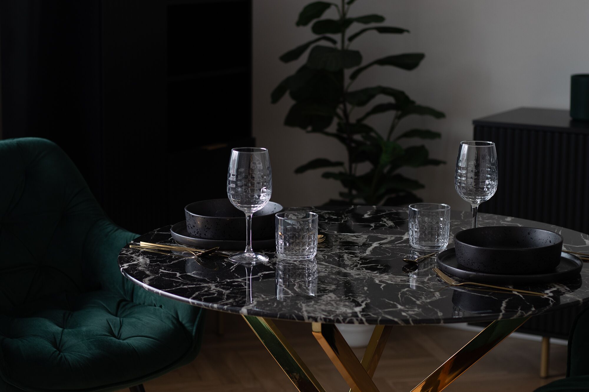 A dining table with four wine glasses and two bowls, a green chair, and a plant in the background.