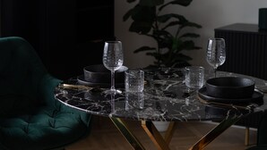 Ein Esstisch mit vier Weingläsern und zwei Schalen, ein grüner Stuhl und eine Pflanze im Hintergrund.