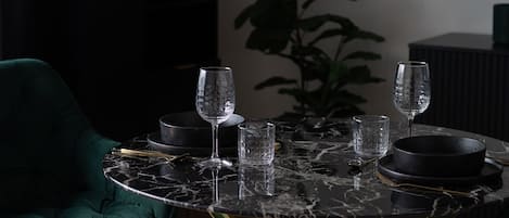 A dining table with four wine glasses and two bowls, a green chair, and a plant in the background.