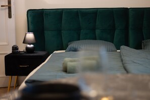 Et soveværelse med en mørkegrøn polstret sengegavl, et natbord med en lampe, og en seng med en stribet pude.