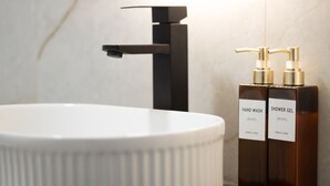 Ein Badezimmer mit einem weißen Waschbecken, einem schwarzen Wasserhahn und zwei braunen Flaschen, beschriftet mit 'HAND WASH' und 'SHOWER GEL'.