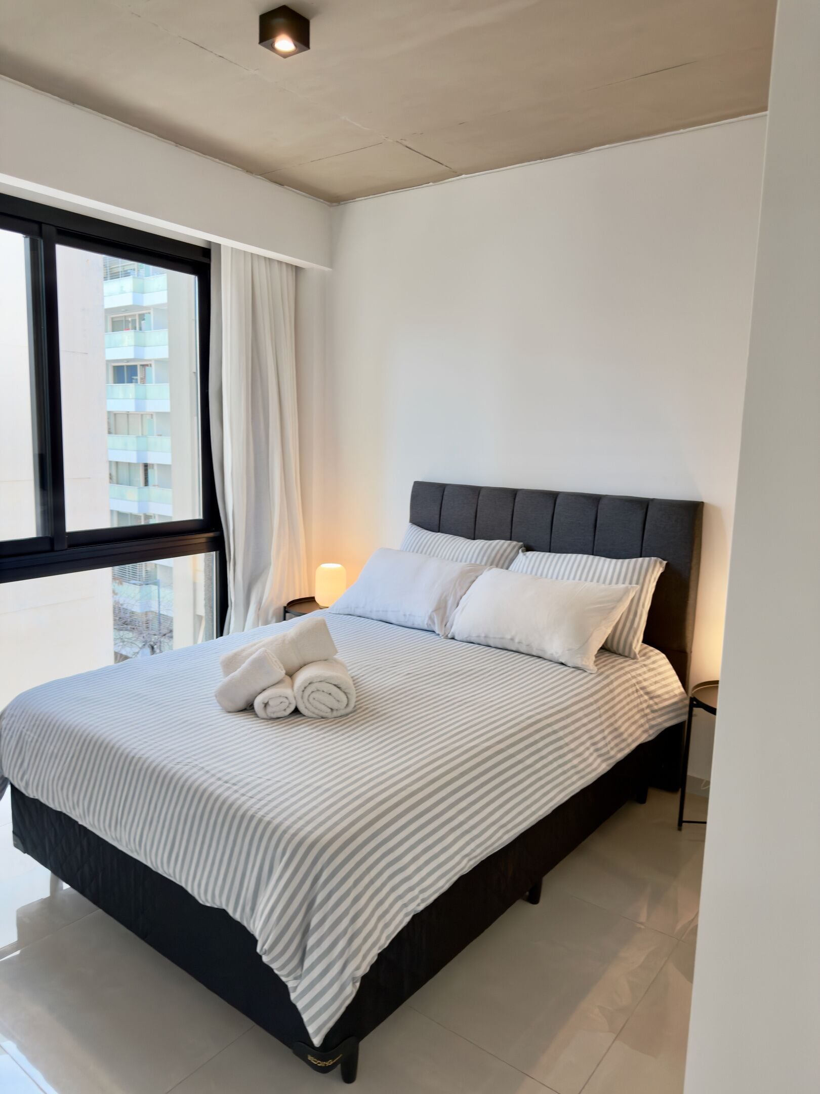 Une chambre à coucher avec un lit, une table de chevet, une lampe et une fenêtre avec des rideaux.
