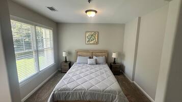 A bedroom with a large bed, two bedside tables, a ceiling light, and a window with blinds.