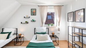 Een moderne slaapkamer met een hoogslaper, twee nachtkastjes, een raam met gordijnen en uitzicht op het omliggende landschap.