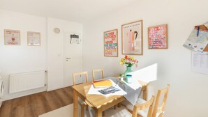 Een eetruimte met een houten tafel, stoelen en een bloevas. Er zijn wanddecoraties en een deur met een klok.