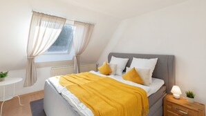 Een slaapkamer met een bed, nachtkastje, lamp en een raam met gordijnen.