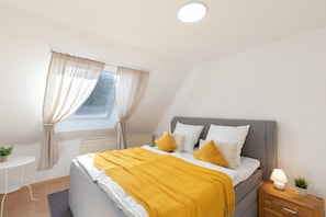 Une chambre à coucher avec un lit, une table de chevet, une lampe et une fenêtre avec des rideaux.