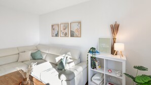 Een moderne woonkamer met een witte bank, een bijzettafeltje en een boekenkast. Er hangen ingelijste foto's aan de muur en op de boekenkast staat een lamp.