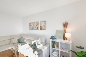 Un salon moderne avec un canapé blanc, une table basse et une bibliothèque. Des tableaux encadrés ornent le mur et une lampe est posée sur la bibliothèque.