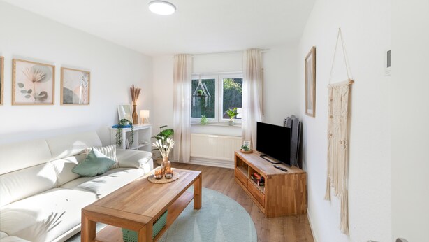 Een woonkamer met een bank, salontafel, tv-meubel en een raam met gordijnen.