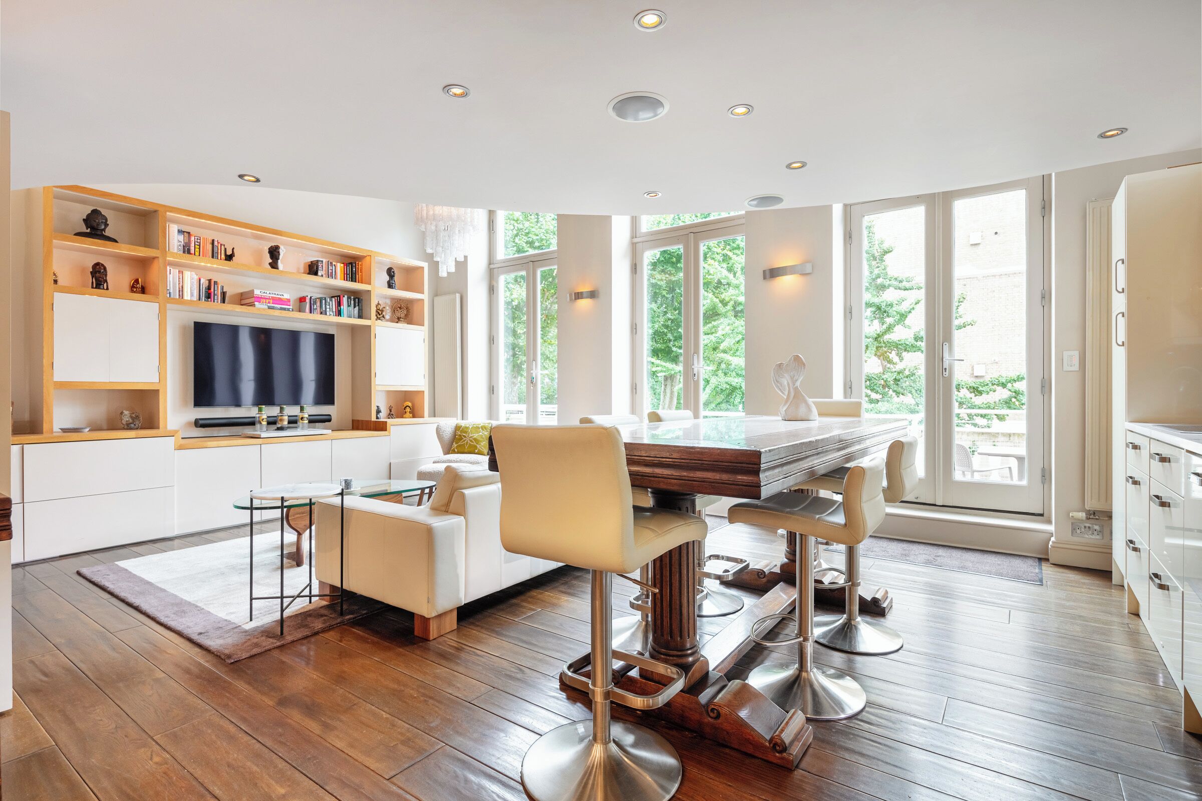 A modern kitchen with a dining area, wooden shelves, and a large window.