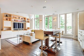 A modern kitchen with a dining area, wooden shelves, and a large window. - Elegant Earls Court Apartment | Loft Bedroom | Lift Access (London)