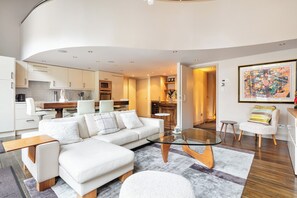 Ein modernes Wohnzimmer mit einem weißen Sofa, einem Glastisch und einem Essbereich mit Holztisch und Stühlen.