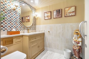 Un baño con un salpicadero de azulejos estampados, un espejo grande, un lavamanos con mueble dorado y una estatua.