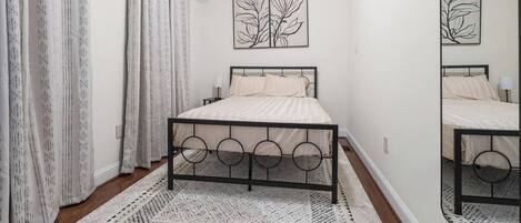 Een slaapkamer met een bed, gordijnen, een vloerkleed en wanddecoratie.