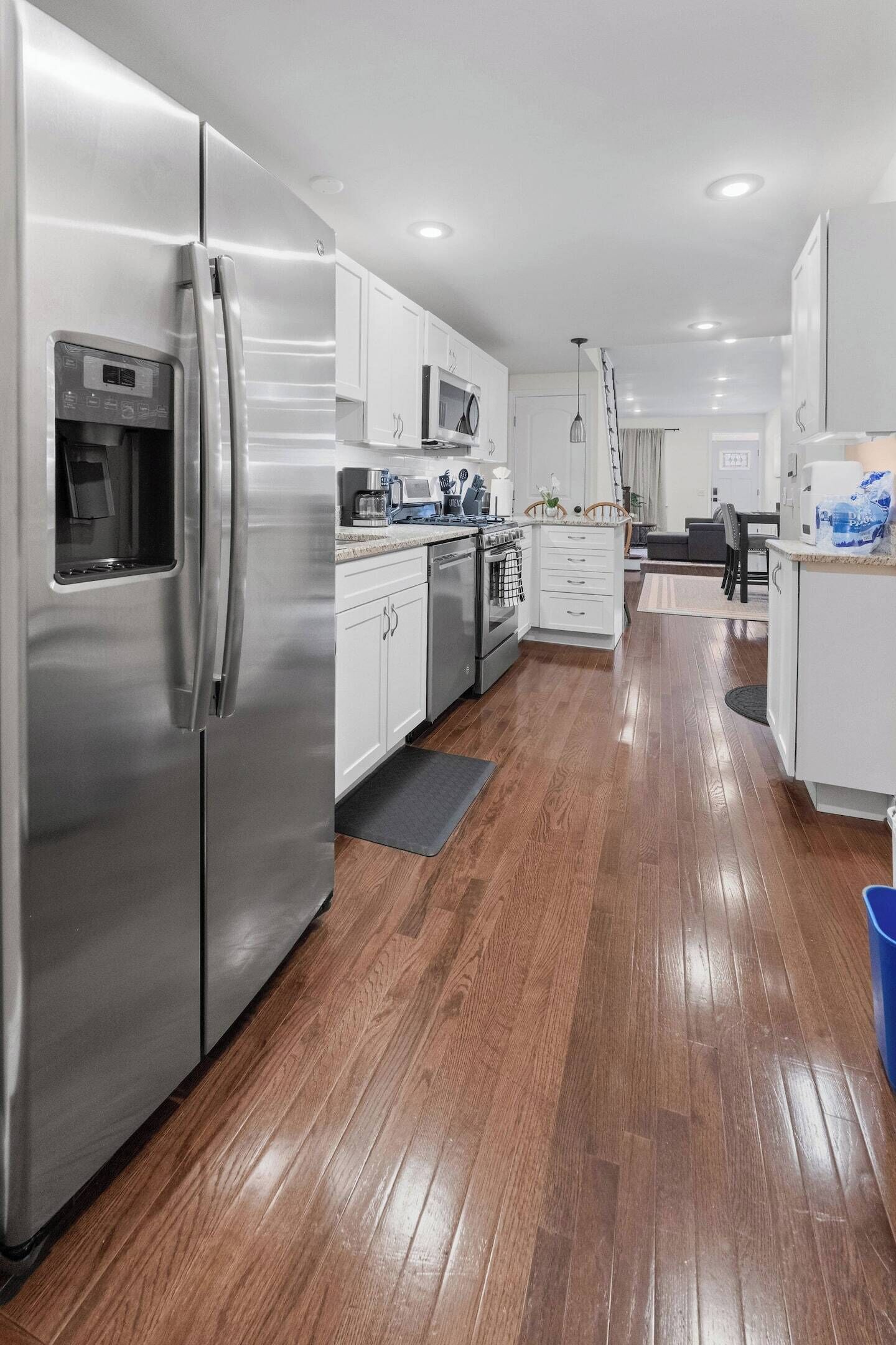 A modern kitchen with stainless steel appliances, white cabinetry, and a wooden floor.