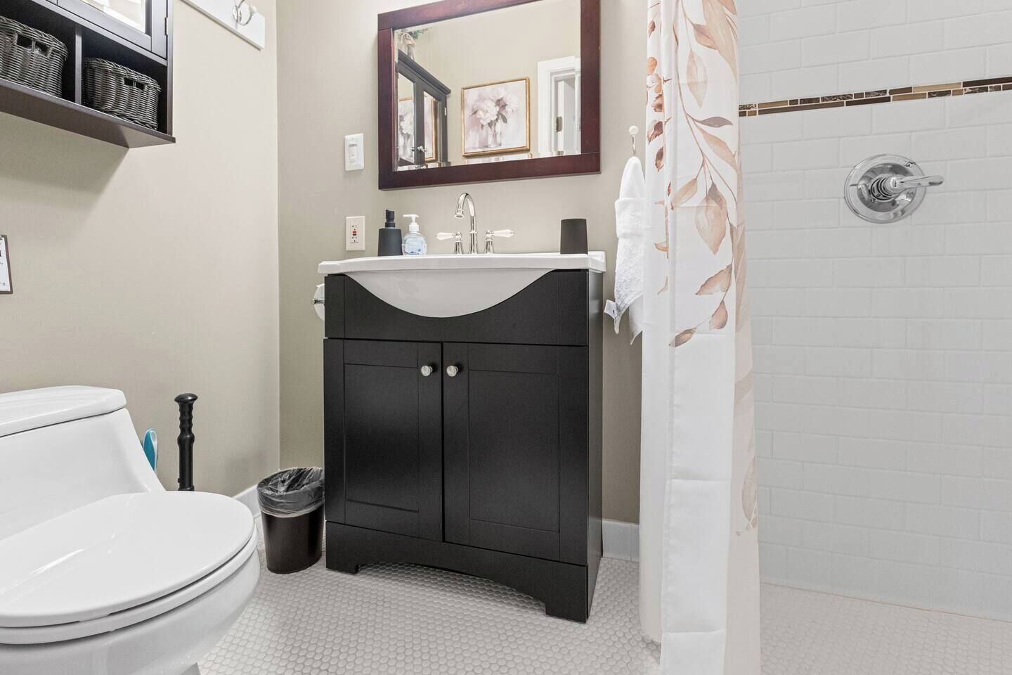 A bathroom with a white toilet, a black vanity with a mirror, and a shower with a floral curtain.